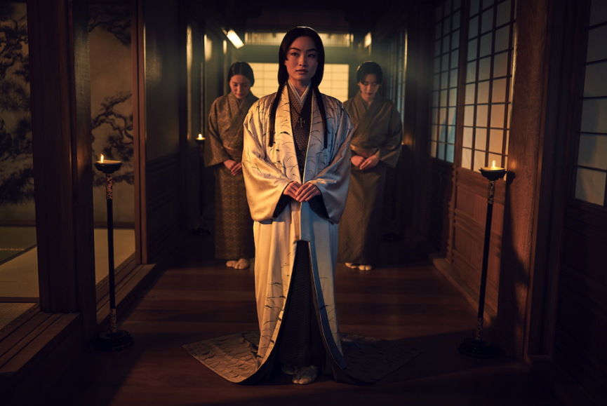 A person in a long robe standing in a hallway with other people behind her

Description automatically generated