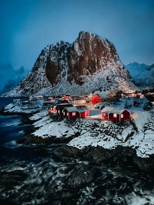 Aldea con casas rojas entre el mar y una montaña nevada.